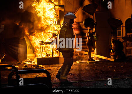 Silhouette di un vigile del fuoco cercando di controllare un incendio in una strada nel corso di una notte. Foto Stock