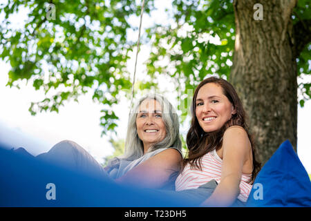 Ritratto di due donne sorridenti rilassante su un letto sospeso in giardino Foto Stock