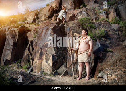 Primitivo persone vestite di pelle di animale vicino alla grotta antica disegno in montagna Foto Stock