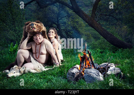 Grotta di persone vestite di pelle di animale seduto vicino a falò in foresta Foto Stock