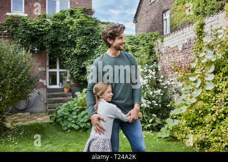 Padre sorridente con la figlia in piedi nel giardino della loro casa Foto Stock