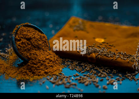 Close up di cumino in polvere o zeera o jeera con cumino grezzo su una superficie di legno in un vaso di argilla su un panno o un tovagliolo. Foto Stock