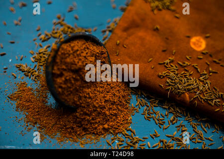 Close up di cumino in polvere o zeera o jeera con cumino grezzo su una superficie di legno in un vaso di argilla su un panno o un tovagliolo. Foto Stock