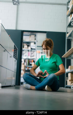 Donna incinta seduta sul pavimento in ufficio avente una pausa Foto Stock