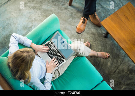 Vista superiore della imprenditrice lavorando sul computer portatile sul lettino di turchese in coworking space Foto Stock