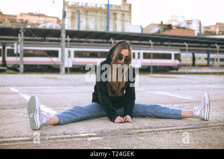 Ritratto di moda giovane donna che indossa gli occhiali da sole e nero giacca con cappuccio Foto Stock
