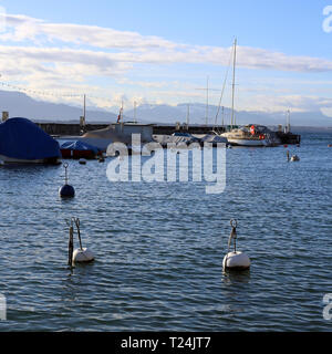 Bellissimo paesaggio fotografato nella pittoresca città di Nyon, Svizzera. In questa foto si vede un lago blu cielo con alcune nuvole, barche e boe. Foto Stock