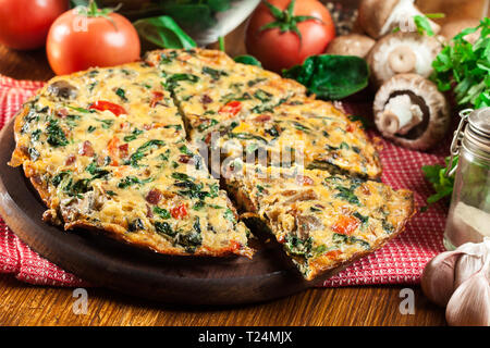 Frittata fatta di uova, funghi e spinaci su un tagliere. Cucina italiana Foto Stock