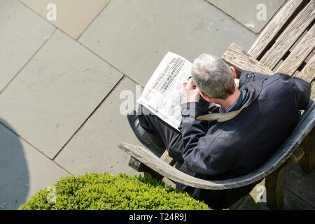 Un solitario grigio uomo dai capelli leggendo un giornale di Londra, Regno Unito Foto Stock