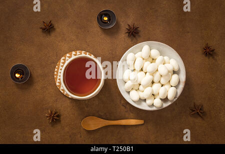 Il tè e le mandorle al cioccolato bianco su sfondo marrone, decorato con candele e spezie. Foto Stock