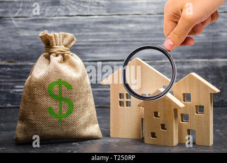 Lente di ingrandimento è guardando le tre case nei pressi di un sacchetto di denaro. Acquisto di beni immobili e di investimento. Convenienti a buon mercato Prestito, ipoteca. Tasse, Foto Stock