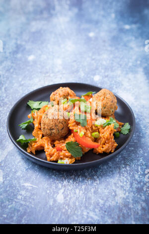 Vista laterale del vegan jambalaya e esotico piatto di riso. Falafels sulla sommità di riso al buio su un piccolo piatto e uno sfondo grigio. Cuocere i falafel jambalaya. Foto Stock