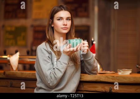 Immagine della donna in grigio felpa con tazza di caffè seduti vicino al tavolo di legno. Foto Stock