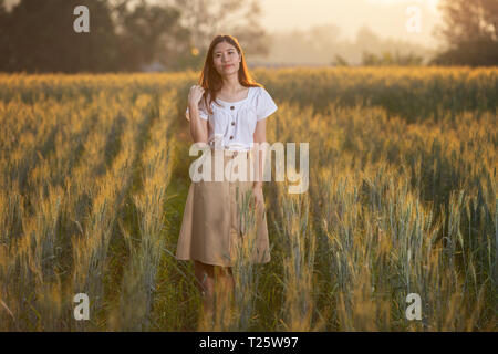 Bella donna asiatica divertendosi al campo di orzo in estate al tramonto Foto Stock