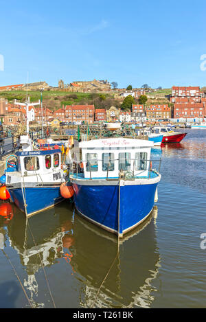 Due piccole barche da pesca nel porto di Whitby riflessa nell'acqua. Gli edifici sono a distanza e non vi è un chiaro cielo blu sopra. Foto Stock