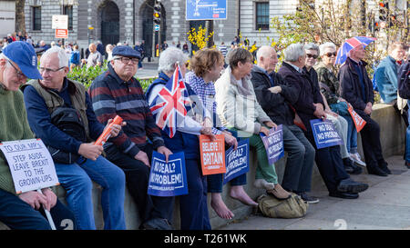 Westminster, Londra, Regno Unito; 29 marzo 2019; Fila di manifestanti Pro-Brexit sedersi su una parete durante il mese di marzo a lasciare Rally. Più tenere pro-Brexit segni Foto Stock