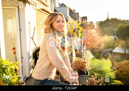 Ritratto di bionda sorridente donna matura in piedi sul balcone in autunno Foto Stock