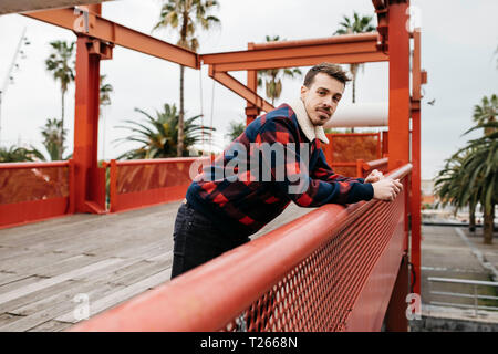 Giovane uomo con abiti casual su un ponte rosso guardando la fotocamera Foto Stock
