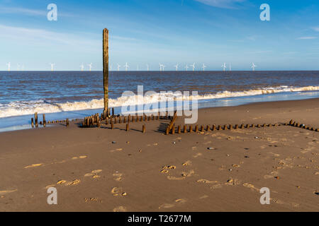 Costa del Mare del Nord in Caister-on-Sea, Norfolk, Inghilterra, Regno Unito - con i resti di un'onda interruttore presso la spiaggia e le turbine eoliche in background Foto Stock