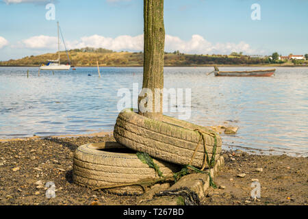 Vecchi pneumatici e un palo di legno nella osono paludi vicino a Faversham Kent, England, Regno Unito - con barche e l'Isle of Sheppey in background Foto Stock