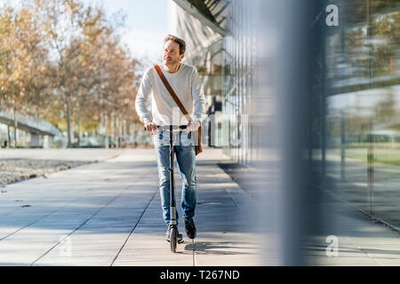 Uomo maturo il pendolarismo nella città, utilizzando kick scooter sul pavemnet Foto Stock