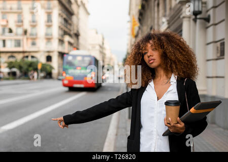Giovane donna con la borsa per notebook e accessori per caffè per andare in città, salutando un taxi Foto Stock
