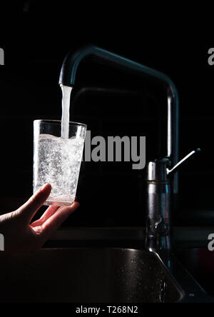 La carenza di acqua. Qualcuno si versa acqua in un bicchiere da un rubinetto in una cucina. Foto Stock