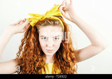 Ritratto di ricci redhead ragazza di colore giallo che indossa la t-shirt raddrizza prua giallo sul suo capo mentre si sta in piedi sul fondo bianco Foto Stock