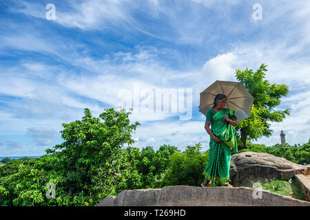 Eleganza presso i monumenti di Mahabalipuram vicino a Chennai, India come una donna passeggiate in campagna, proteggere se stessa dal sole con un ombrellone Foto Stock