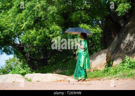 Eleganza presso i monumenti di Mahabalipuram vicino a Chennai, India come una donna passeggiate in campagna, proteggere se stessa dal sole con un ombrellone Foto Stock