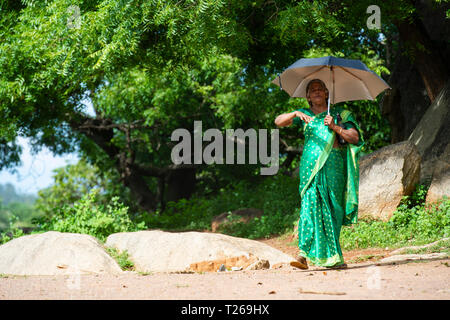 Eleganza presso i monumenti di Mahabalipuram vicino a Chennai, India come una donna passeggiate in campagna, proteggere se stessa dal sole con un ombrellone Foto Stock