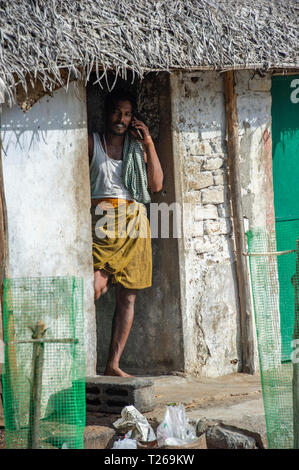 Un uomo che indossa un giubbotto in una baracca chat sul suo telefono cellulare - tecnologia moderna in India in remoto Foto Stock