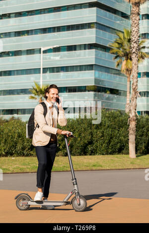 Laughing Man sul telefono con zaino e E-scooter in città Foto Stock