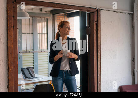 Sorridente imprenditrice avente una pausa caffè in ufficio Foto Stock