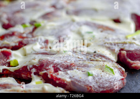 Marinata di pezzi di carni di vitello in salsa bianca di close-up. Raw bistecche di manzo steso su una pietra ardesia bordo con cipolle e spezie. Raw bistecche di manzo con o Foto Stock