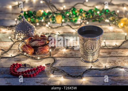 Date, rosario, e acqua cup con Allah scrivere in arabo in background delle luci Foto Stock
