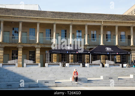 Persona / visitatore / persone / visitatori / turisti sedersi e rilassarsi sui passi al di sotto della parete ovest del quadrangolo del restaurato Piece Hall. Giornata di sole / sun. Halifax, England, Regno Unito Foto Stock