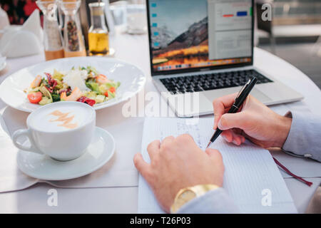 Bella immagine di uomo di mani tenendo la penna. Non ci sono computer portatile, insalata e di caffè al tavolo. Imprenditore ordinato cibo da mangiare. Egli è occupato. Ci sono ope Foto Stock