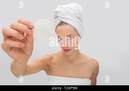 Giovane donna freckled sorge e mostra una spugna bianca vicino alla fotocamera. Guarda. Modello con lentiggini è seirous e concentrata. Indossa white Foto Stock