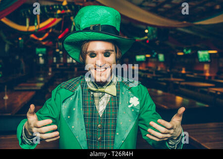 Funny giovane azienda monete sugli occhi e sorriso. Egli stand in pub da solo. Guy sembra felice Foto Stock