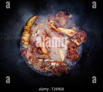 Uzbek riso pilaf il processo di cottura. Agnello in un grande cast-calderone di ferro sul fuoco Foto Stock