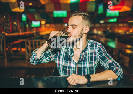 Giovane uomo seduto solitario al bancone bar in pub. Egli bere birra scura da mug Foto Stock