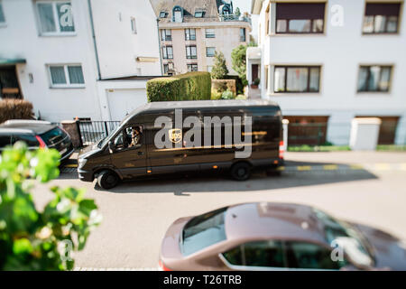 Parigi, Francia - Mar 27, 2019: vista dal di sopra della lasciando marrone di consegna UPS Parcel van sul francese strada residenziale - tilt-shift lente utilizzata shallow focus focus su autista che parla al telefono Foto Stock