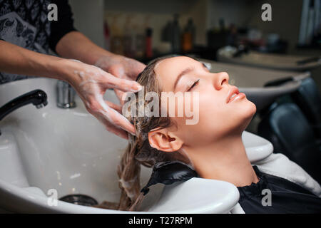 Bella giovane donna seduta vicino al lavandino mentre parrucchiere lavare i capelli in un salone di bellezza. Hair stylist al lavoro Foto Stock