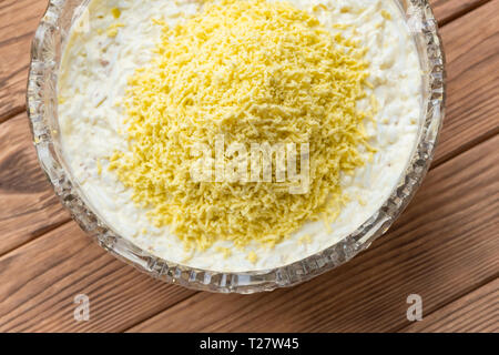 Il processo di cottura del pesce insalata stratificata Mimosa. La posa di scorza di tuorlo d'uovo. Sfondo di legno Foto Stock