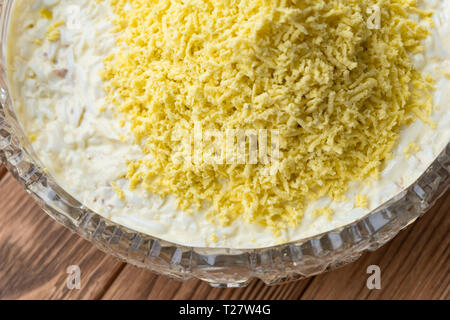 Il processo di cottura del pesce insalata stratificata Mimosa. La posa di scorza di tuorlo d'uovo. Sfondo di legno Foto Stock