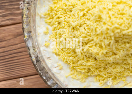 Il processo di cottura del pesce insalata stratificata Mimosa. La posa di scorza di tuorlo d'uovo. Sfondo di legno Foto Stock