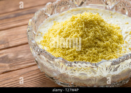 Il processo di cottura del pesce insalata stratificata Mimosa. La posa di scorza di tuorlo d'uovo. Sfondo di legno Foto Stock