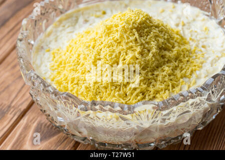 Il processo di cottura del pesce insalata stratificata Mimosa. La posa di scorza di tuorlo d'uovo. Sfondo di legno Foto Stock