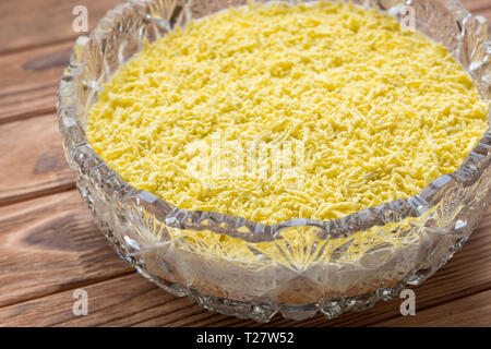 Il processo di cottura del pesce insalata stratificata Mimosa. La posa di scorza di tuorlo d'uovo. Sfondo di legno Foto Stock